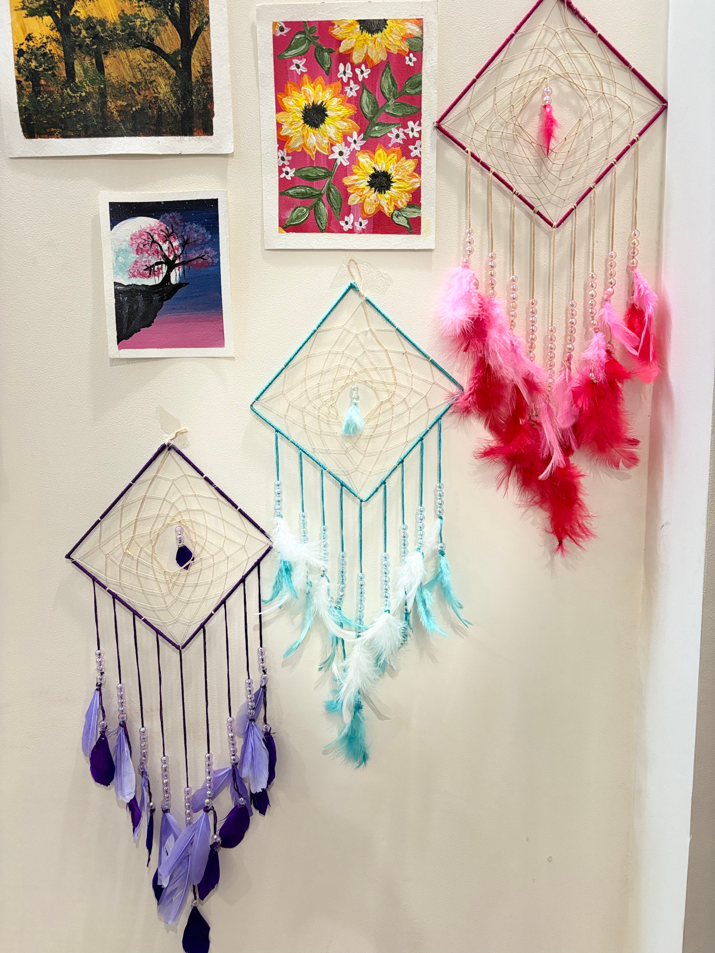 Three handmade dream catchers in purple, teal and pink with feathers and beads