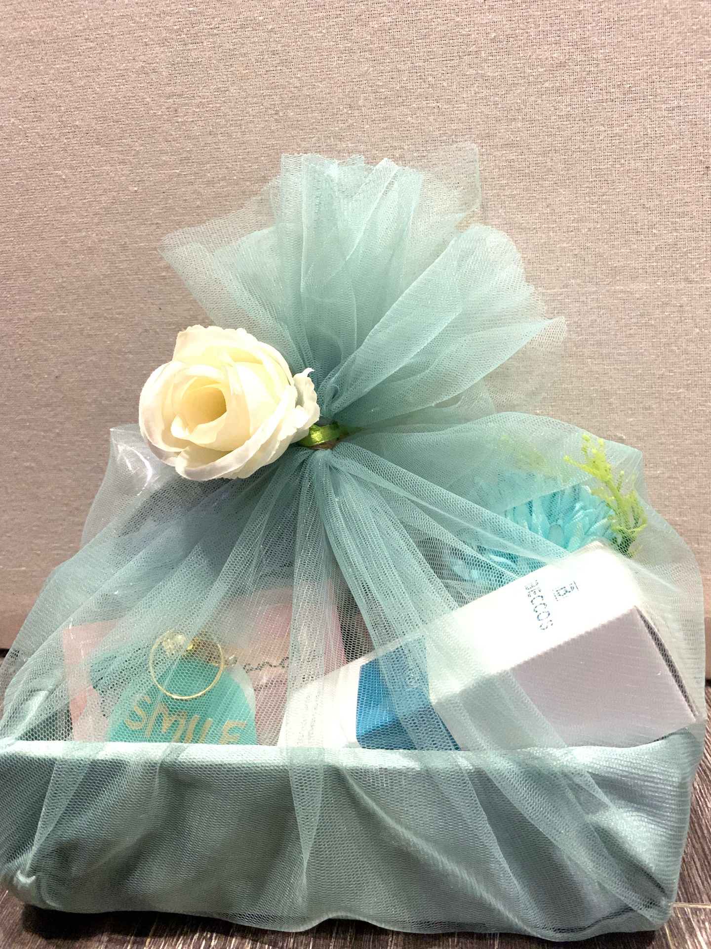 Gift hamper wrapped in mint green tulle with a cream rose